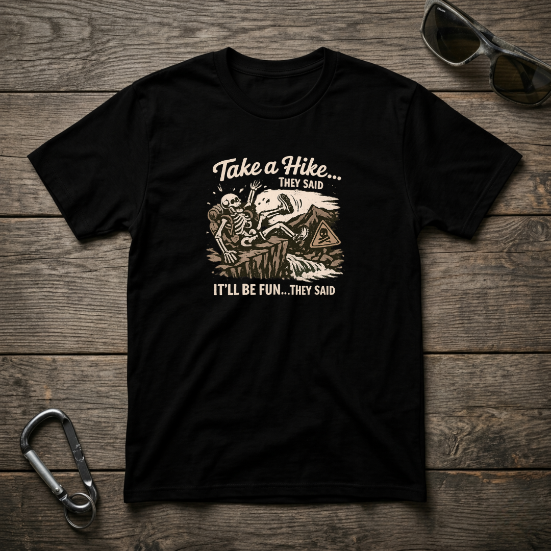 Black graphic T-shirt from Designed For The Wild Co featuring "Take a Hike They Said" text in a casual, garment-dyed style.