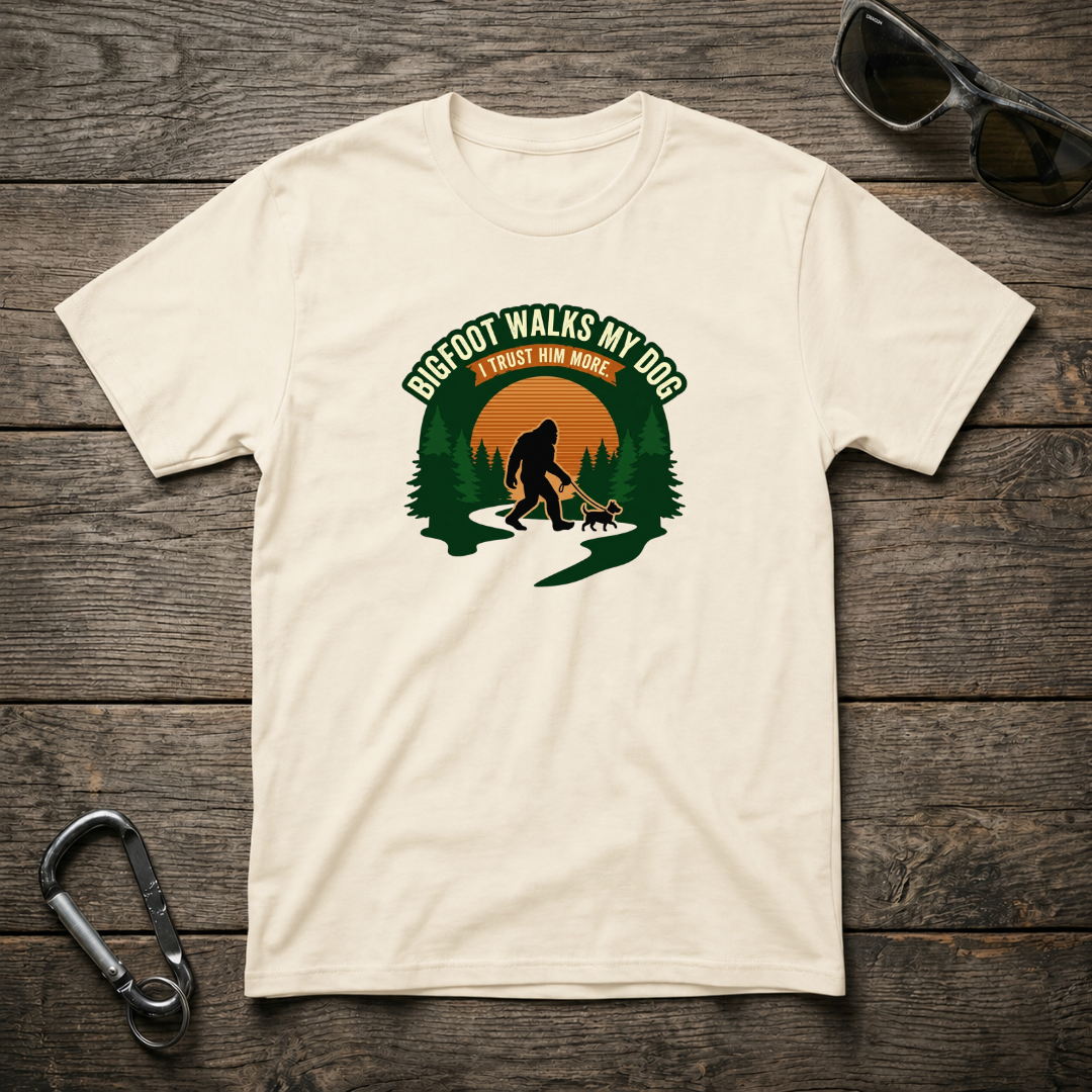 Bigfoot walks with a dog in a graphic T-shirt by Designed For The Wild Co, featuring a nature-inspired design on a softstyle fabric.