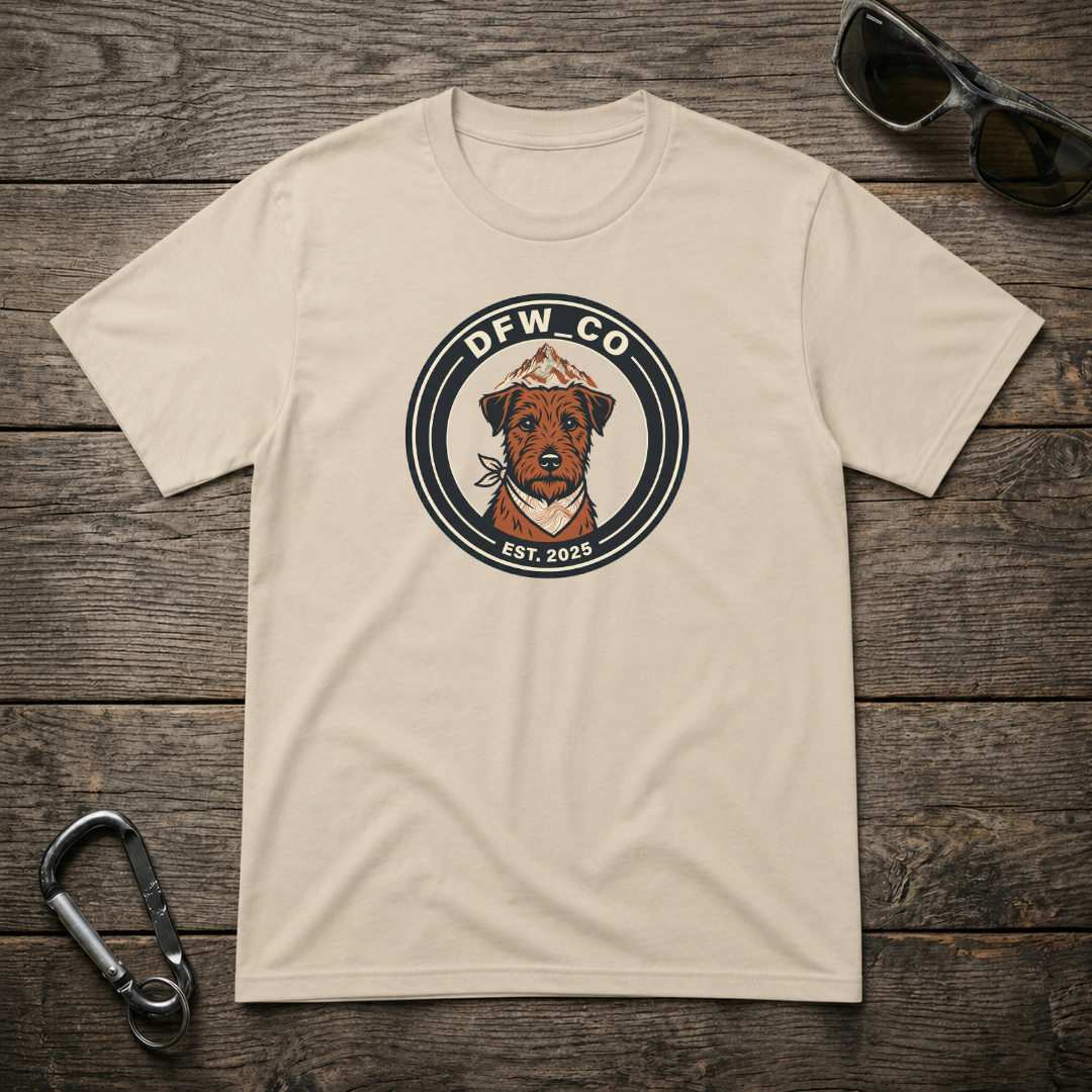 Designed For The Wild Co Schnauzer Trail Club graphic heavyweight T-shirt with a rugged outdoor design on sand-colored fabric.