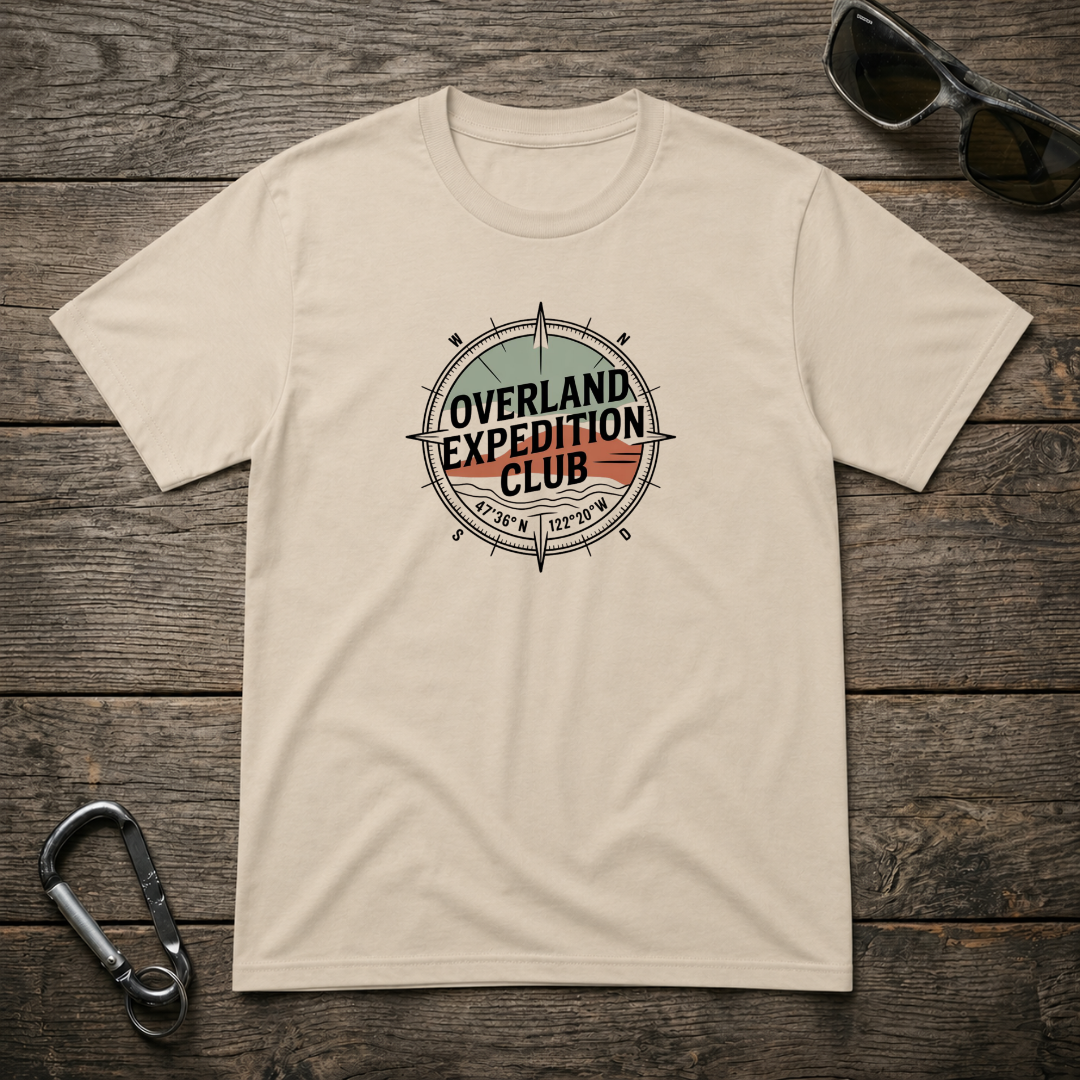 Designed For The Wild Co Overland Expedition heavyweight graphic T-shirt featuring rugged outdoor-inspired artwork on a sandy background.