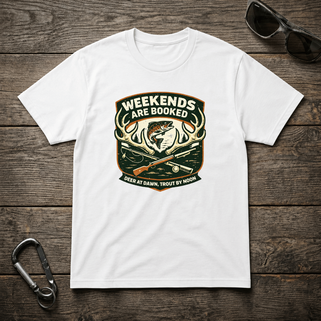White graphic T-shirt from Designed For The Wild Co featuring "Weekends Are Booked Camping" text and outdoor-themed design.