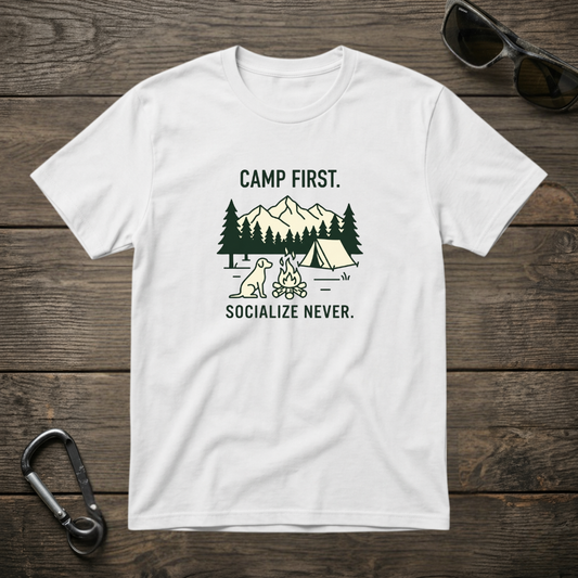 White graphic T-shirt by Designed For The Wild Co with "Camp First, Socialize Never" slogan, garment-dyed cotton tee.